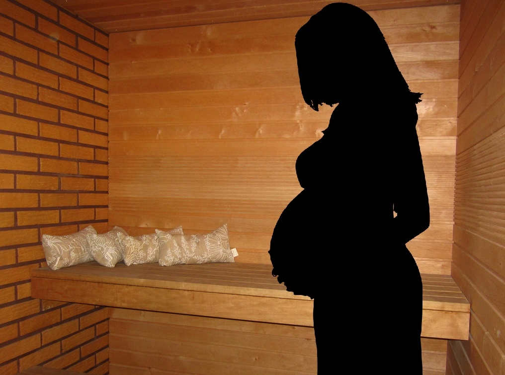 pregnant woman holding her belly in front of a sauna